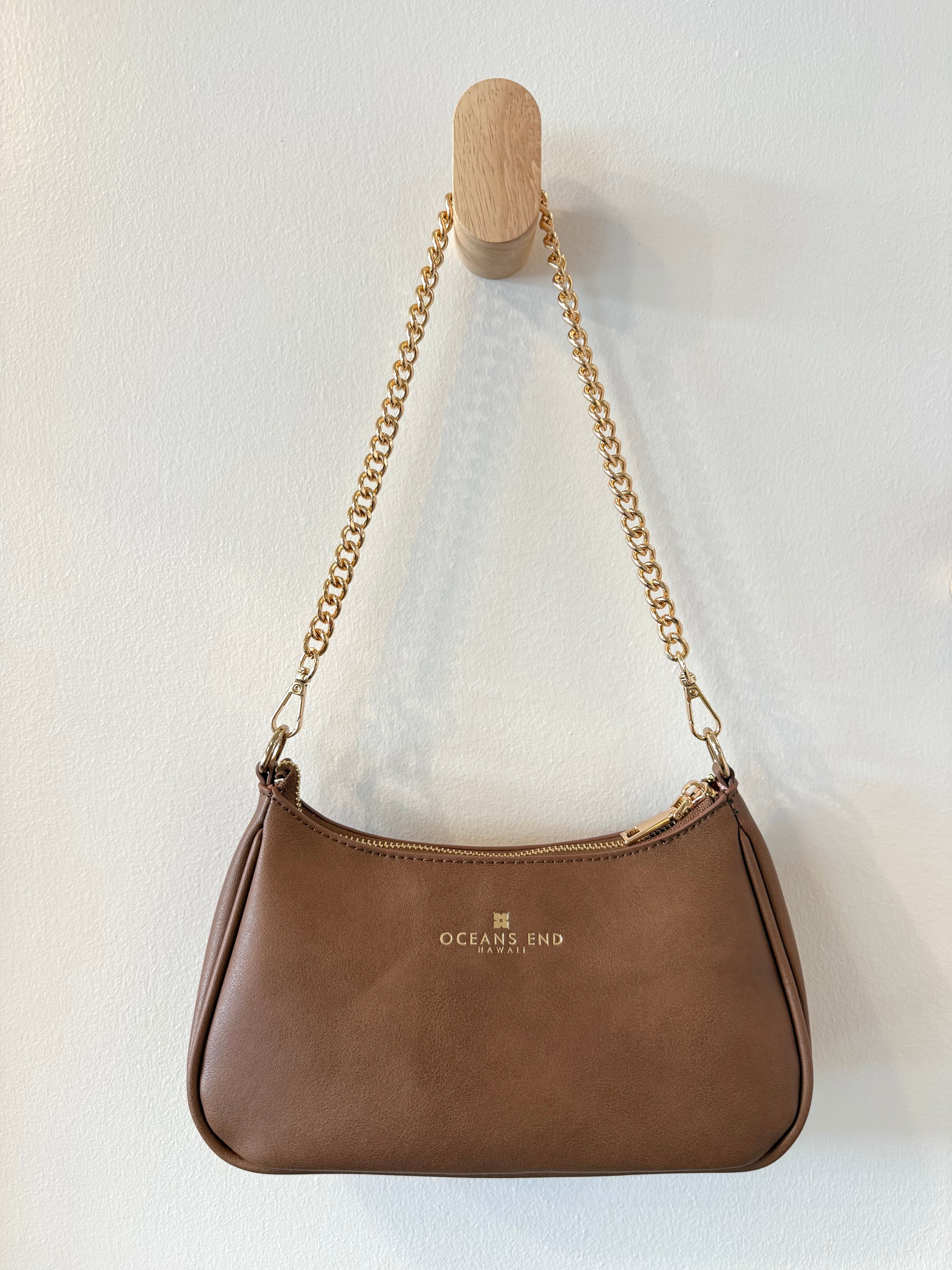 the back of our mocha shylynn bag displayed with our oceans end logo at the top center hanging from a gold chain shoulder strap.