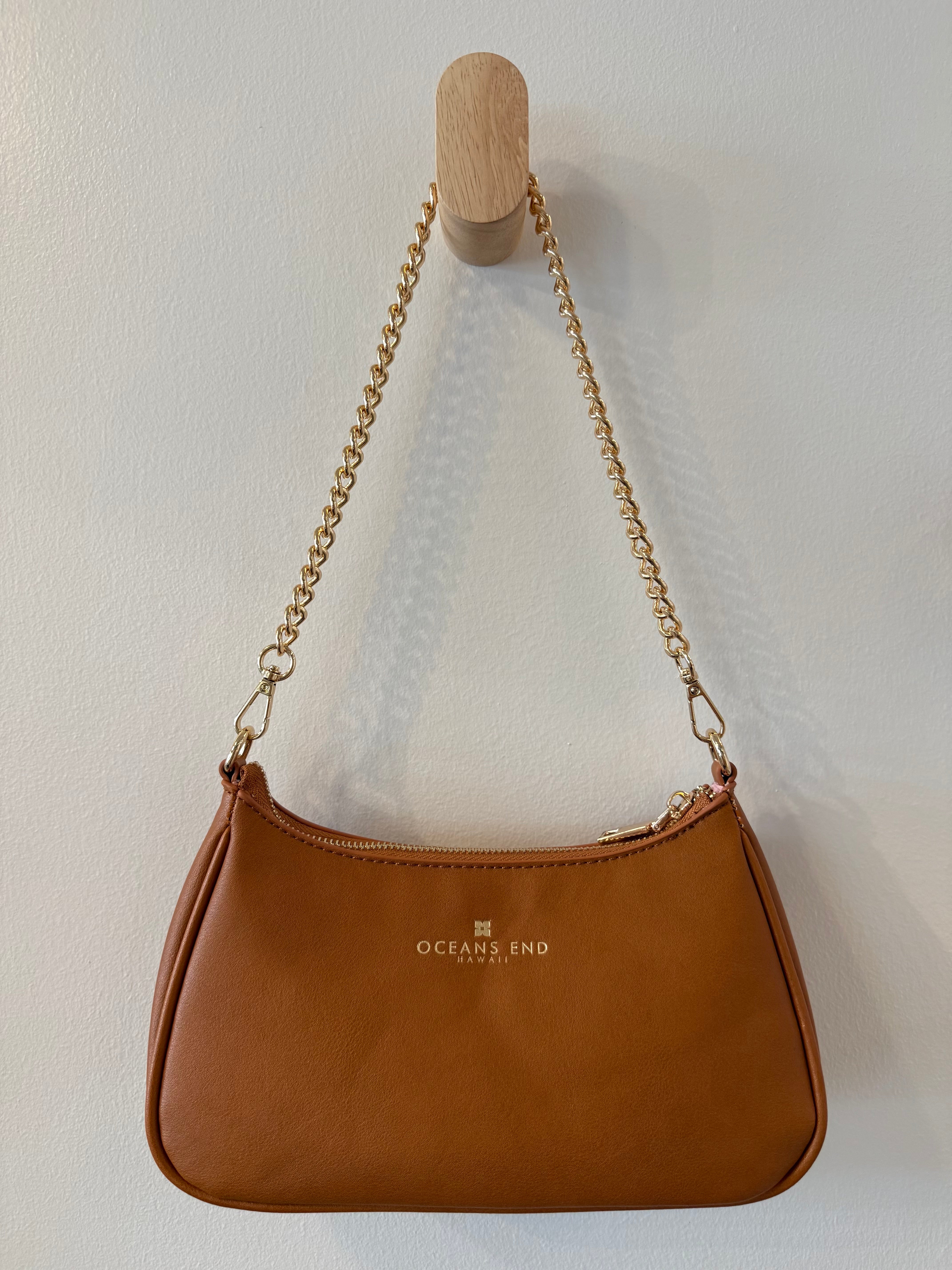 the back of our brown shylynn bag displayed with our oceans end logo at the top center hanging from a gold chain shoulder strap.