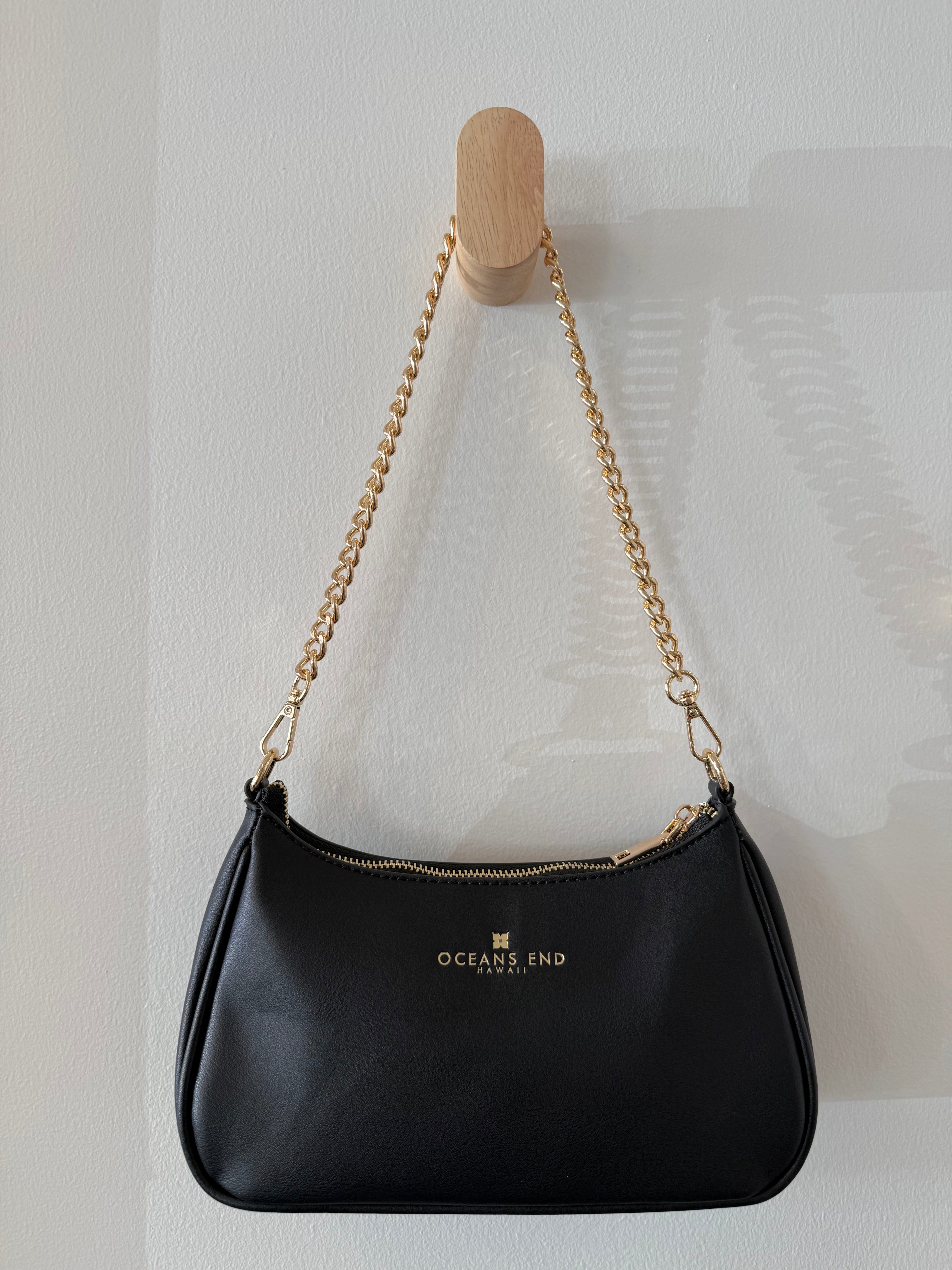 the back of our black shylynn bag displayed with our oceans end logo at the top center hanging from a gold chain shoulder strap.