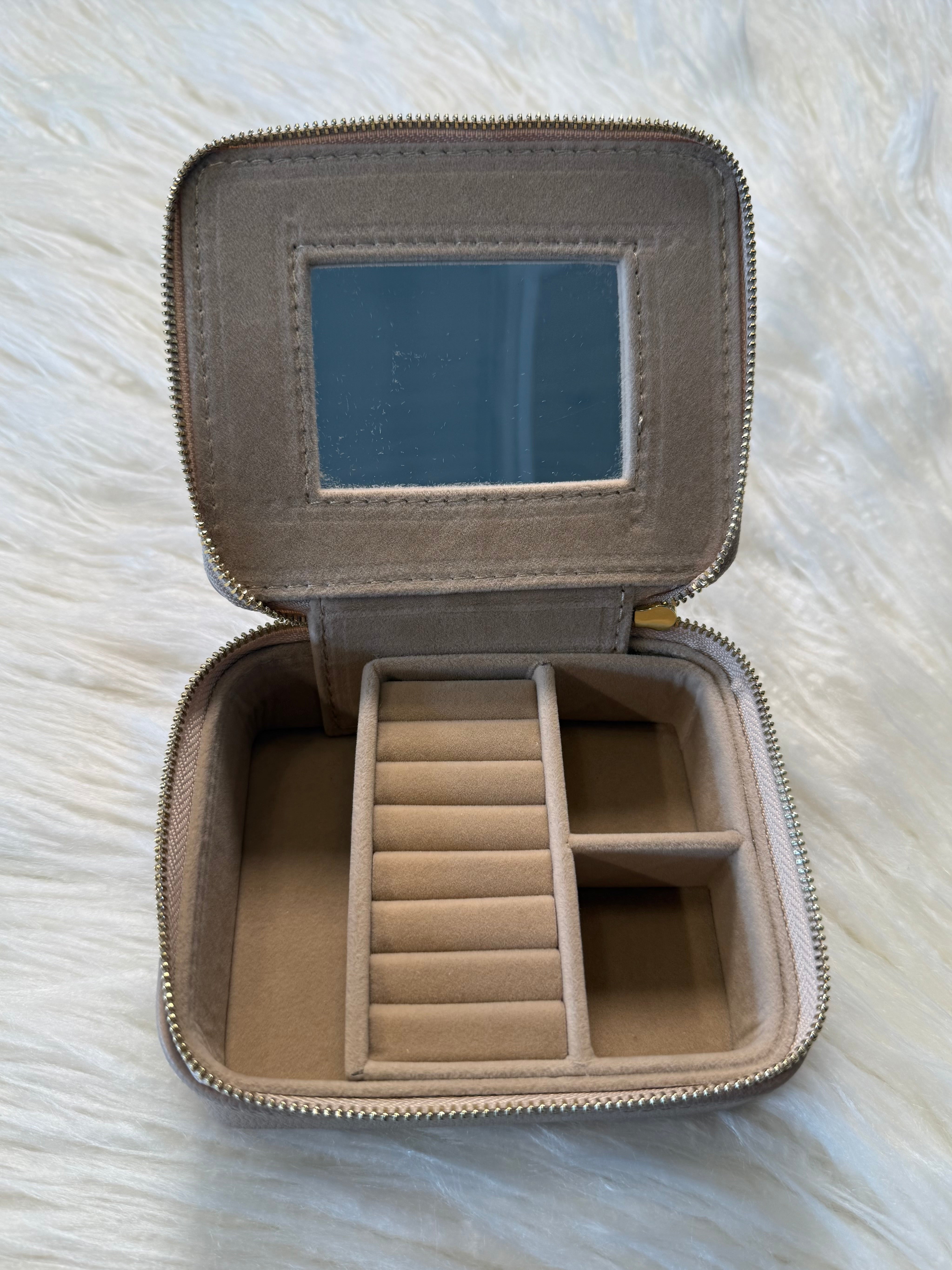 Compact jewelry case open showing the inside featuring a built in mirror on the lid, ring rolls, 3 open compartments and a gold zip closure.